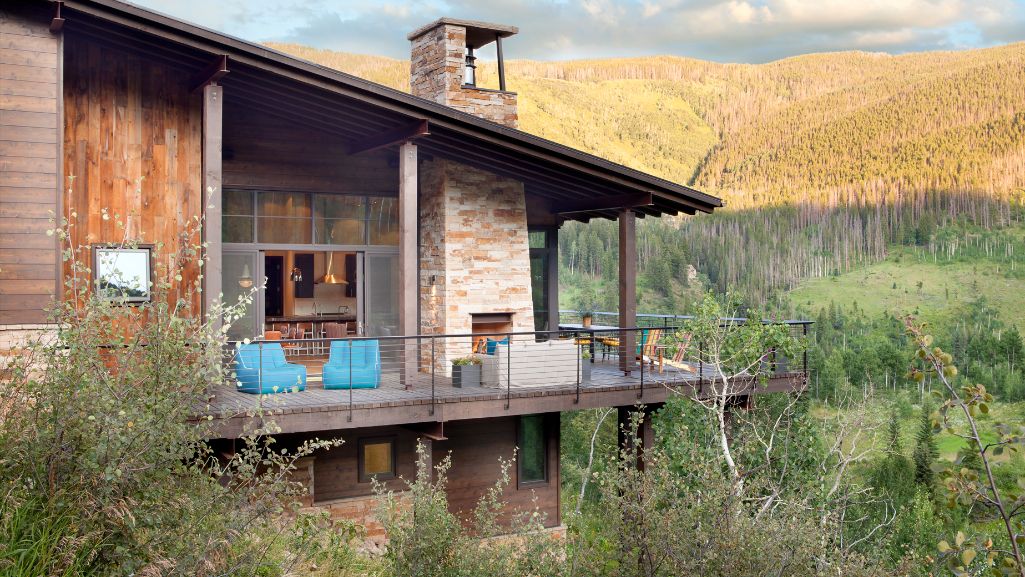 A wooden house with a large porch in the middle of a forest.