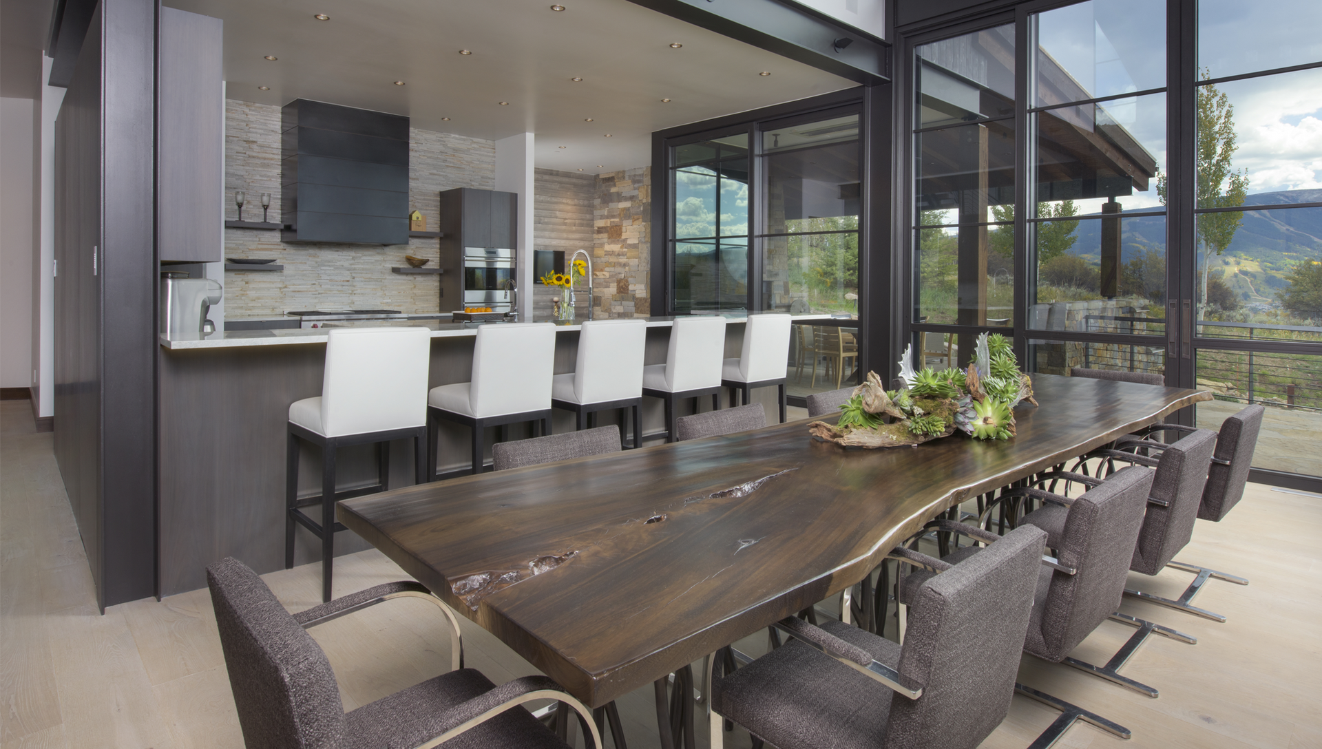 A dining room table with chairs and a kitchen in the background.