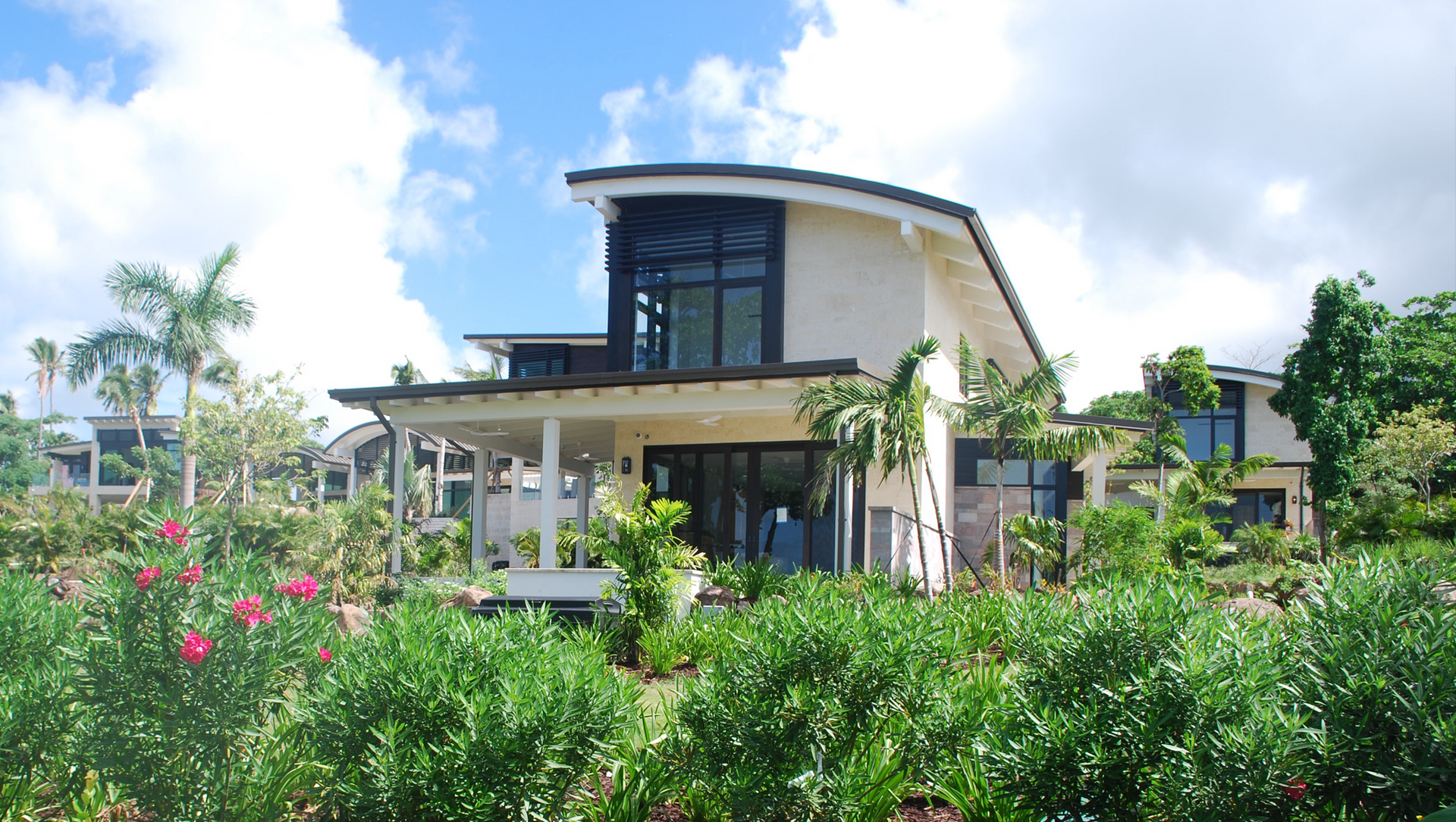 A large house with a curved roof is surrounded by bushes and trees