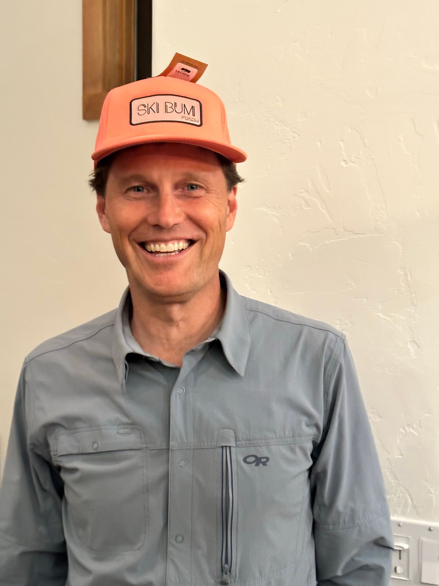 A man wearing a hat and a gray shirt is smiling.