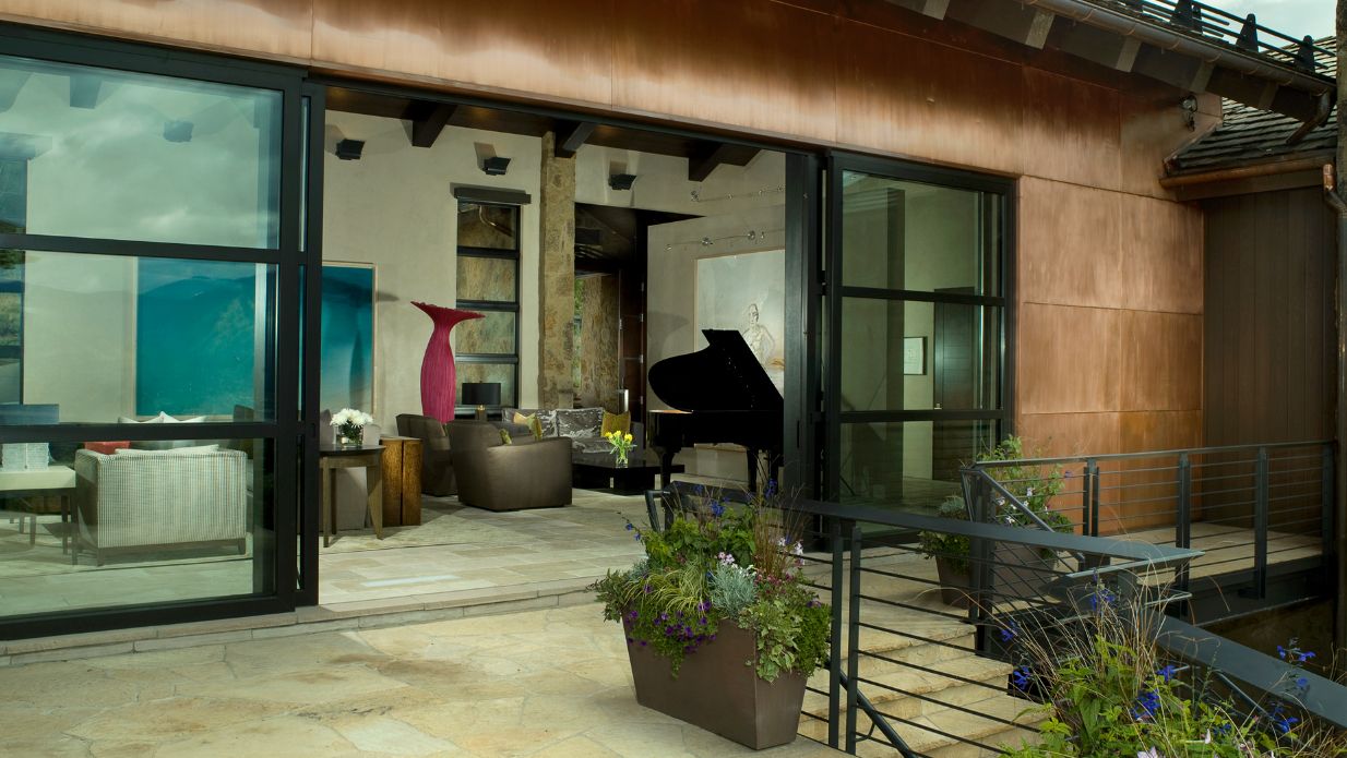 A large sliding glass door opens to a patio with a piano in the background.