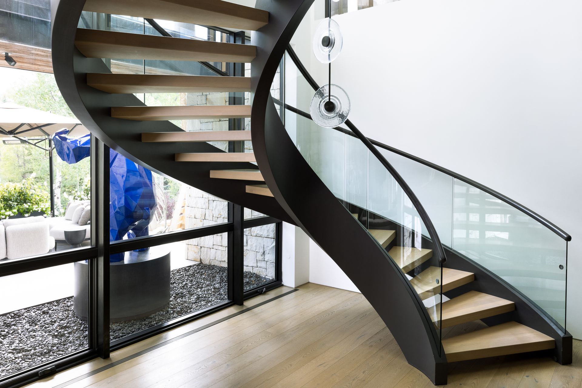 A modern spiral staircase with wooden steps and a glass railing