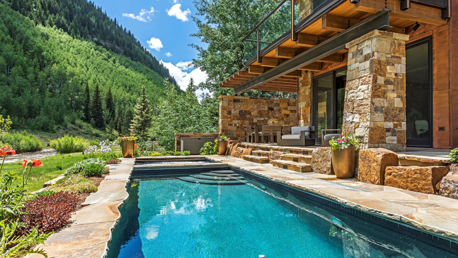 There is a large swimming pool in front of a house with mountains in the background.