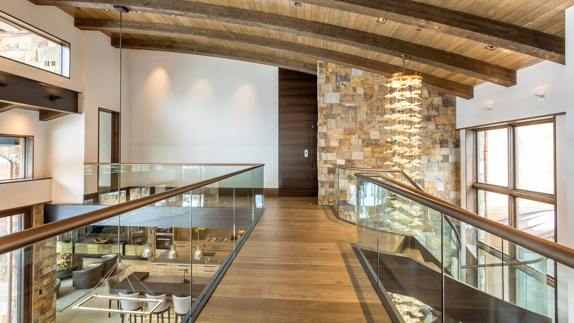 A hallway in a house with a glass railing and wooden beams.