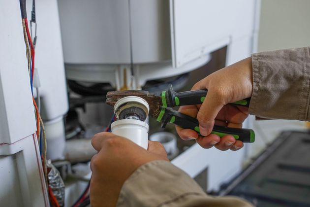 Hands using pliers to install a white plumbing pipe under a sink.