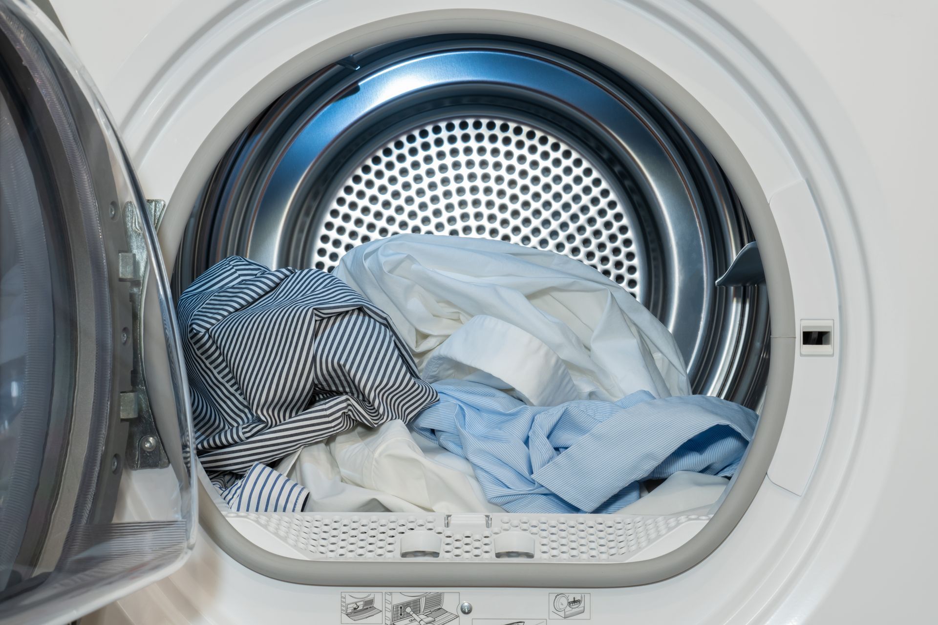 Open washing machine drum filled with striped and white laundry
