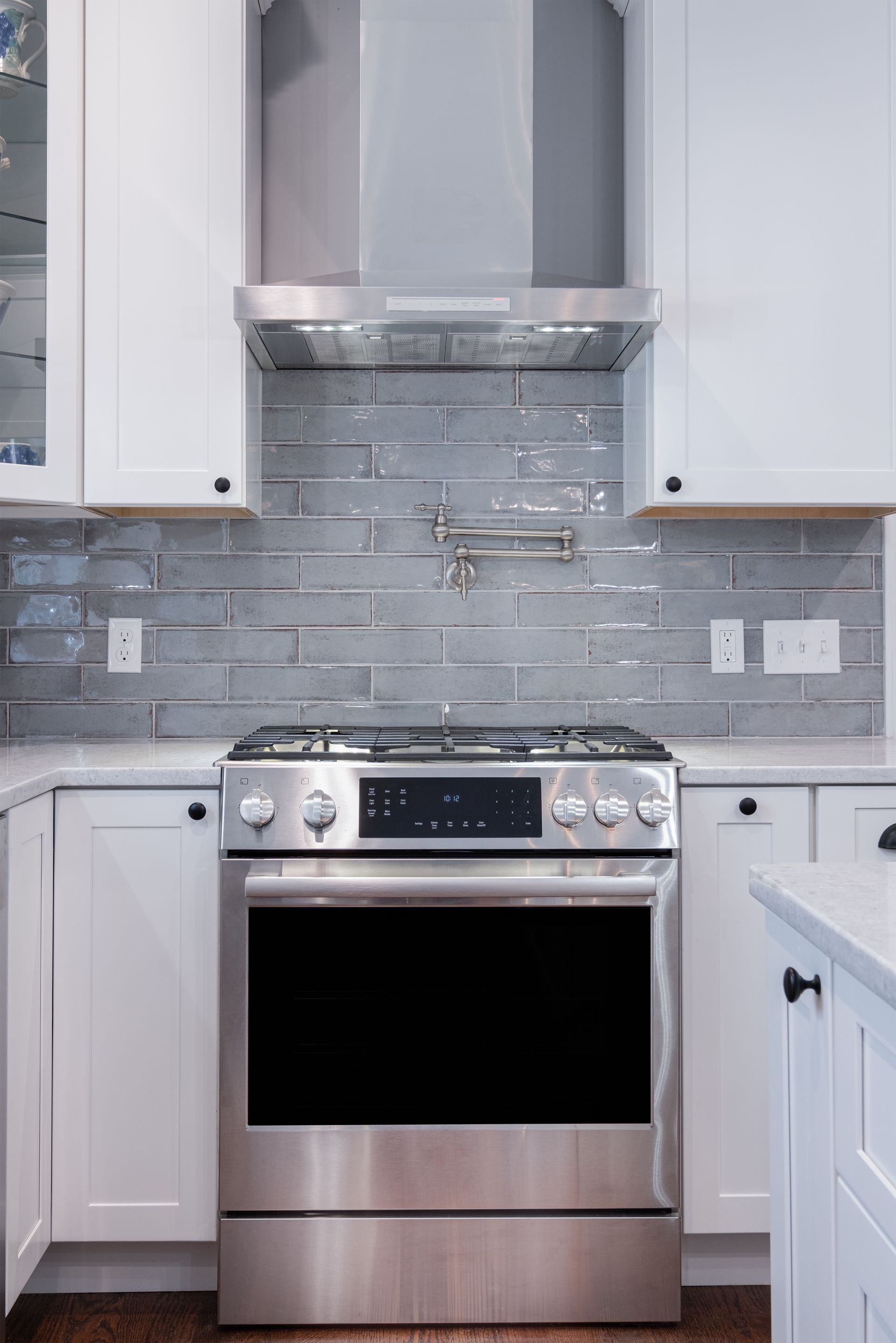 Modern kitchen with stainless steel stove, white cabinets, and gray tile backsplash
