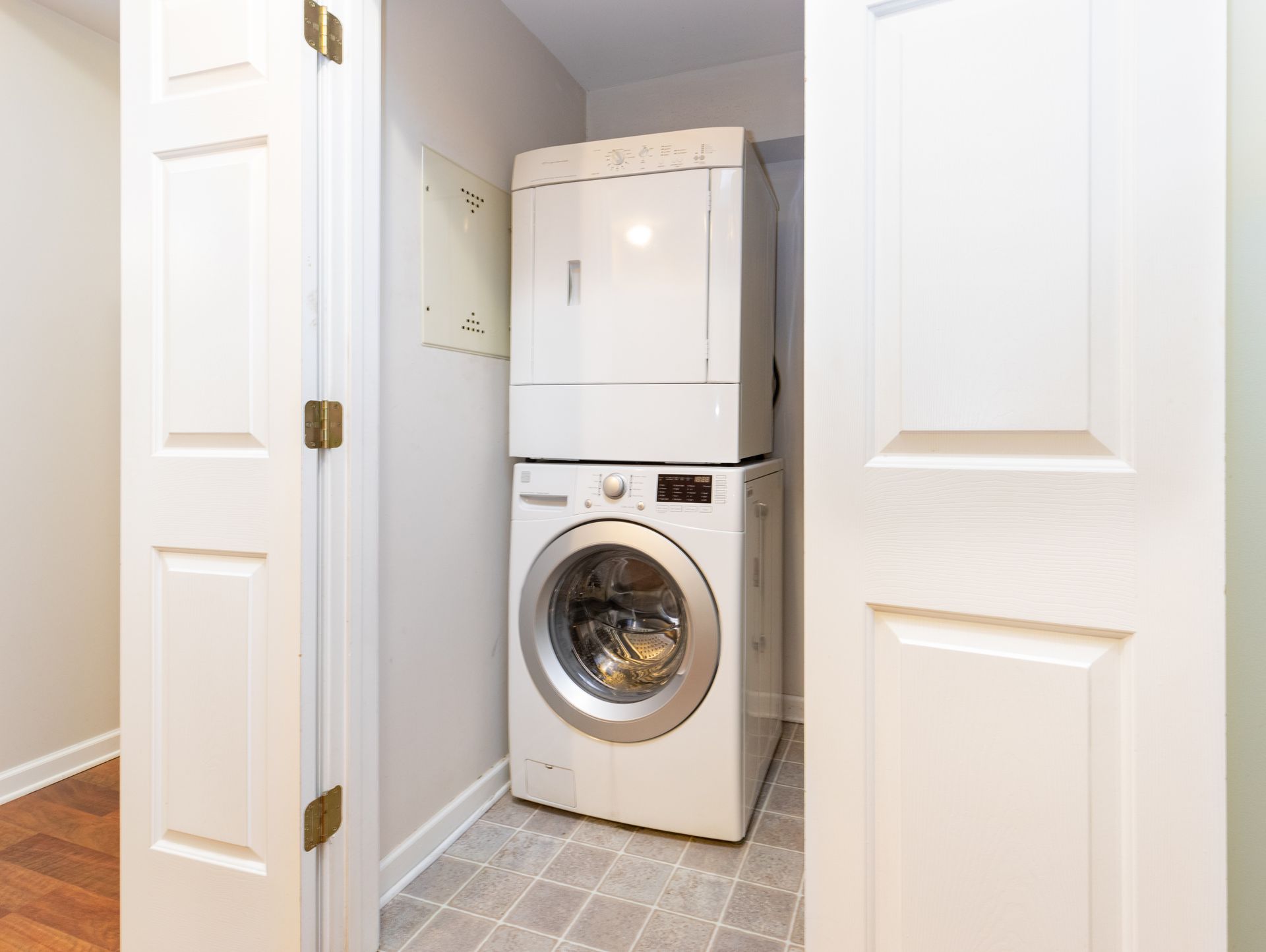 Stacked washer and dryer in a narrow laundry closet with white louvered doors open