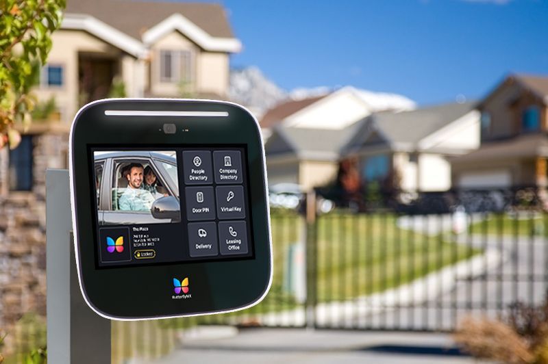 A ButterflyMX video intercom installed on a pedestal at a suburban gated entrance.