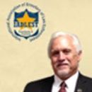 A man in a suit and tie smiling beside the blue and gold IADLEST organization logo.