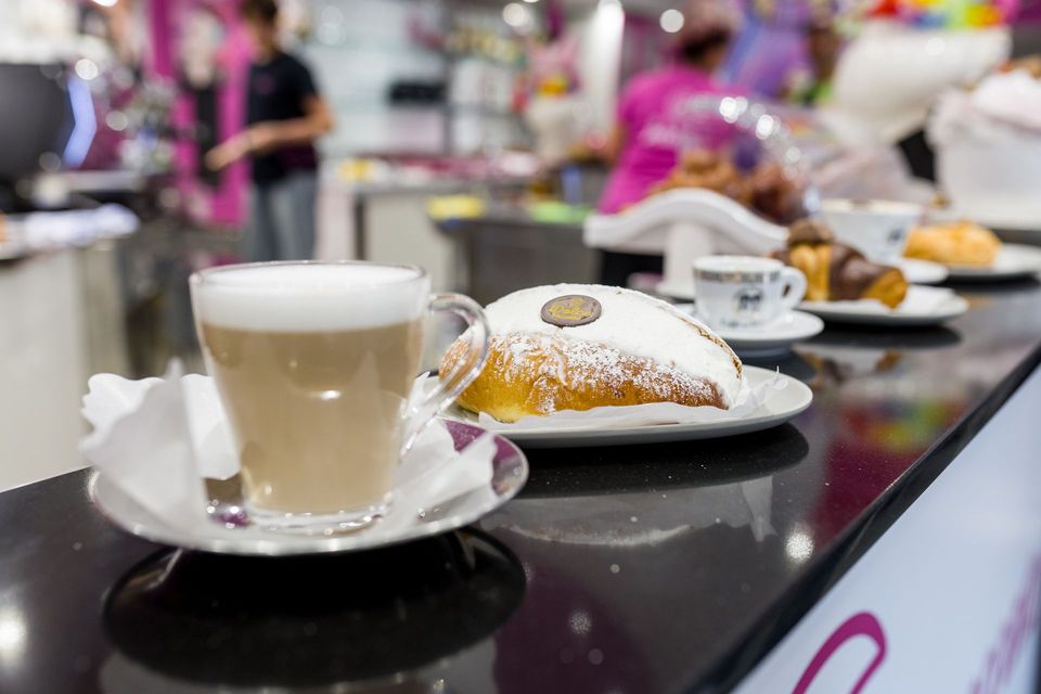 Cappuccino e pasta frolla in polvere su un bancone in un bar affollato.