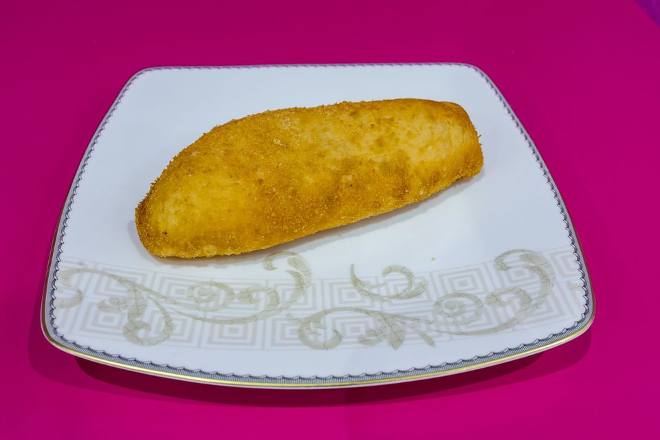Pasta fritta dorata su un piatto bianco decorato, su uno sfondo rosa acceso.