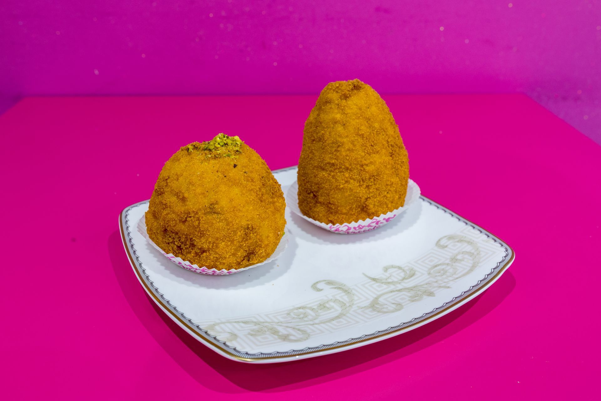 Due snack fritti gialli su un piatto bianco su uno sfondo rosa acceso