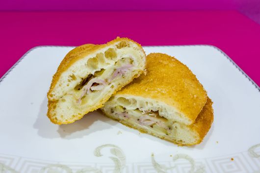 Due metà di un panino ripieno impanato su un piatto bianco su sfondo rosa