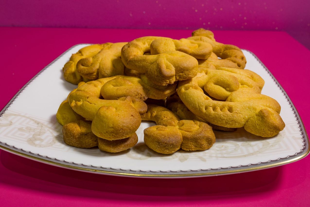 Un piatto di pasticcini dorati fritti su un piatto bianco su uno sfondo rosa acceso.