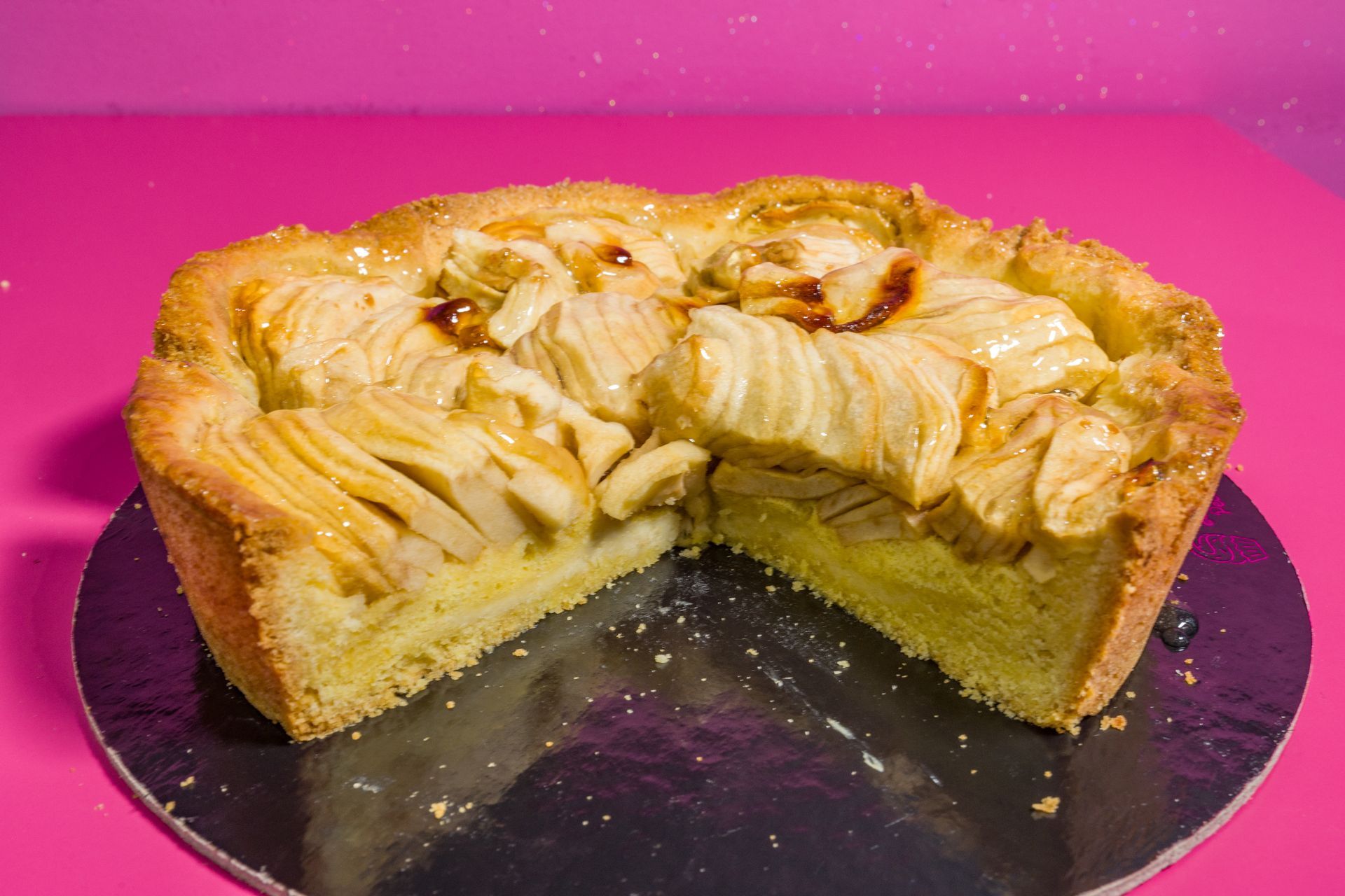 Torta di mele con frutta a fette su un piatto nero su uno sfondo rosa acceso.