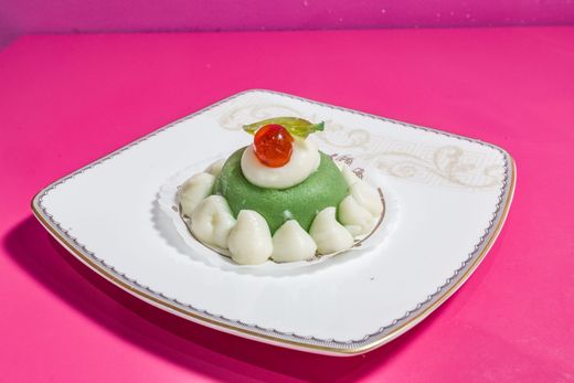 Dessert guarnito con panna e ciliegie su un piatto bianco su sfondo rosa.
