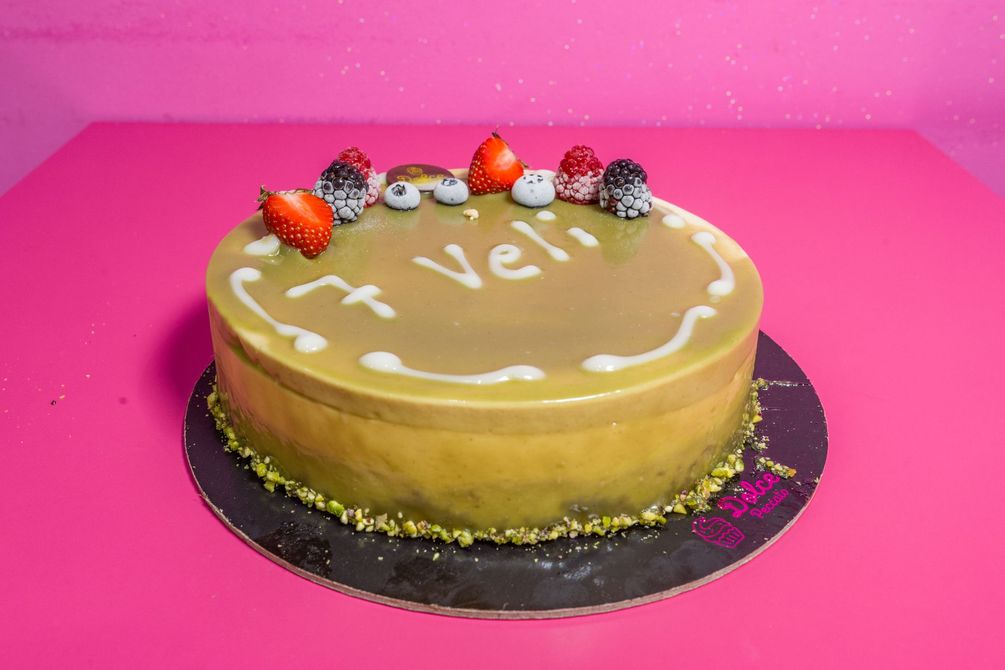 Torta al cioccolato con messaggio in glassa bianca e frutti di bosco su un tavolo rosa.