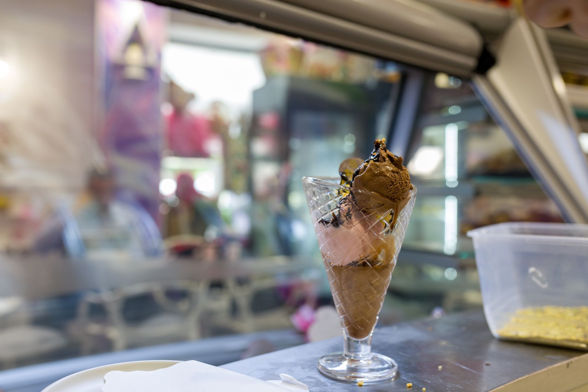 Coppa di gelato al cioccolato in un bicchiere su un bancone, con uno sfondo sfocato di un bar.