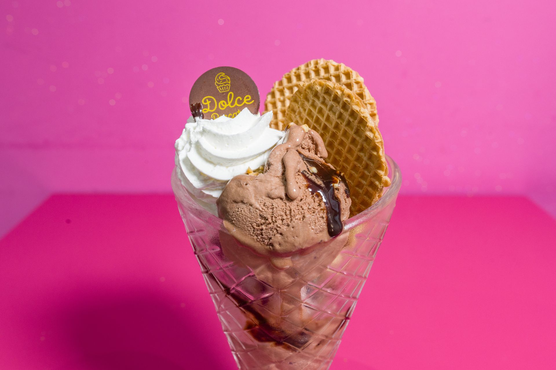 Gelato al cioccolato in un cono con panna montata e cialda su sfondo rosa
