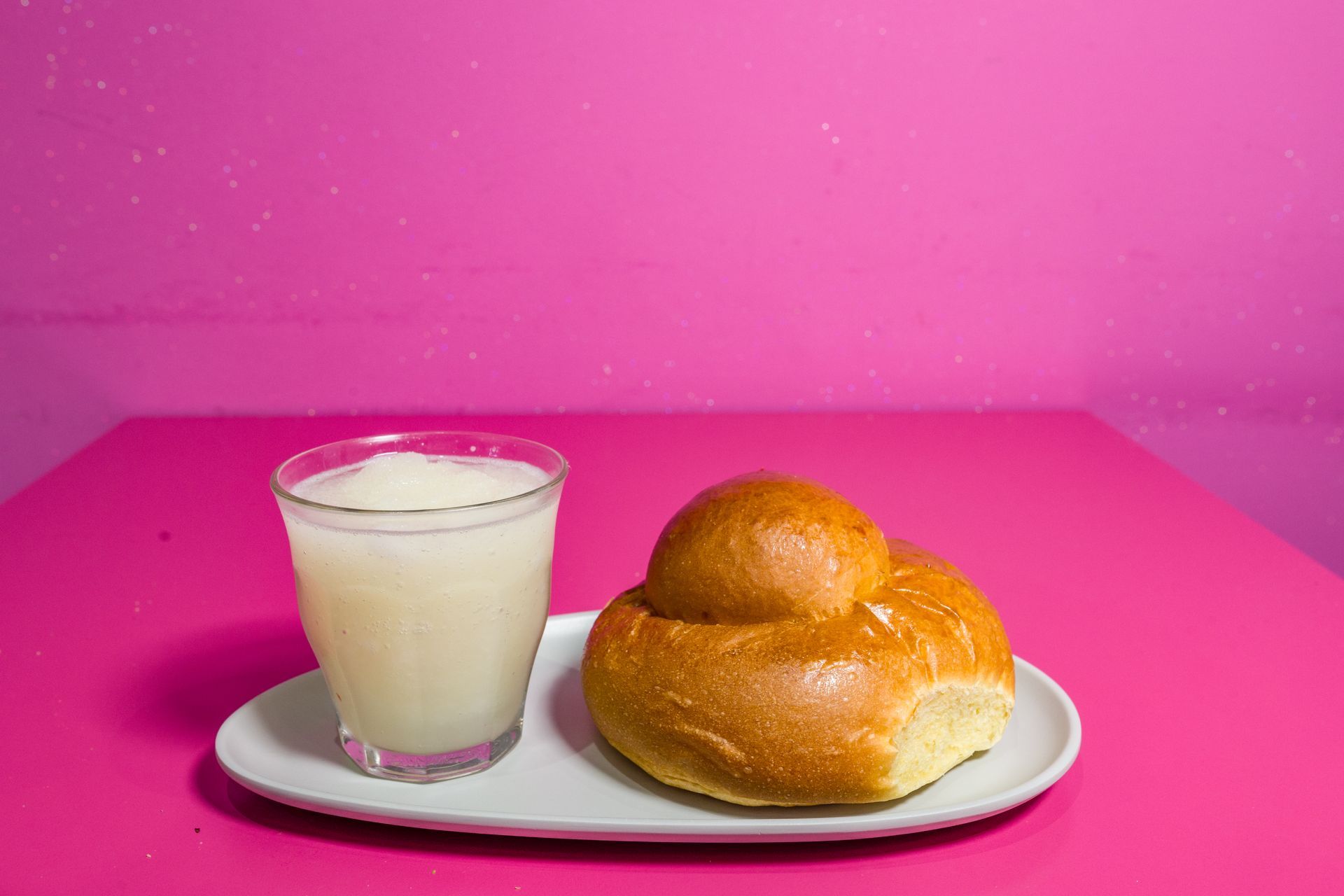 Un bicchiere di latte e due panini su un piatto bianco su uno sfondo rosa acceso.
