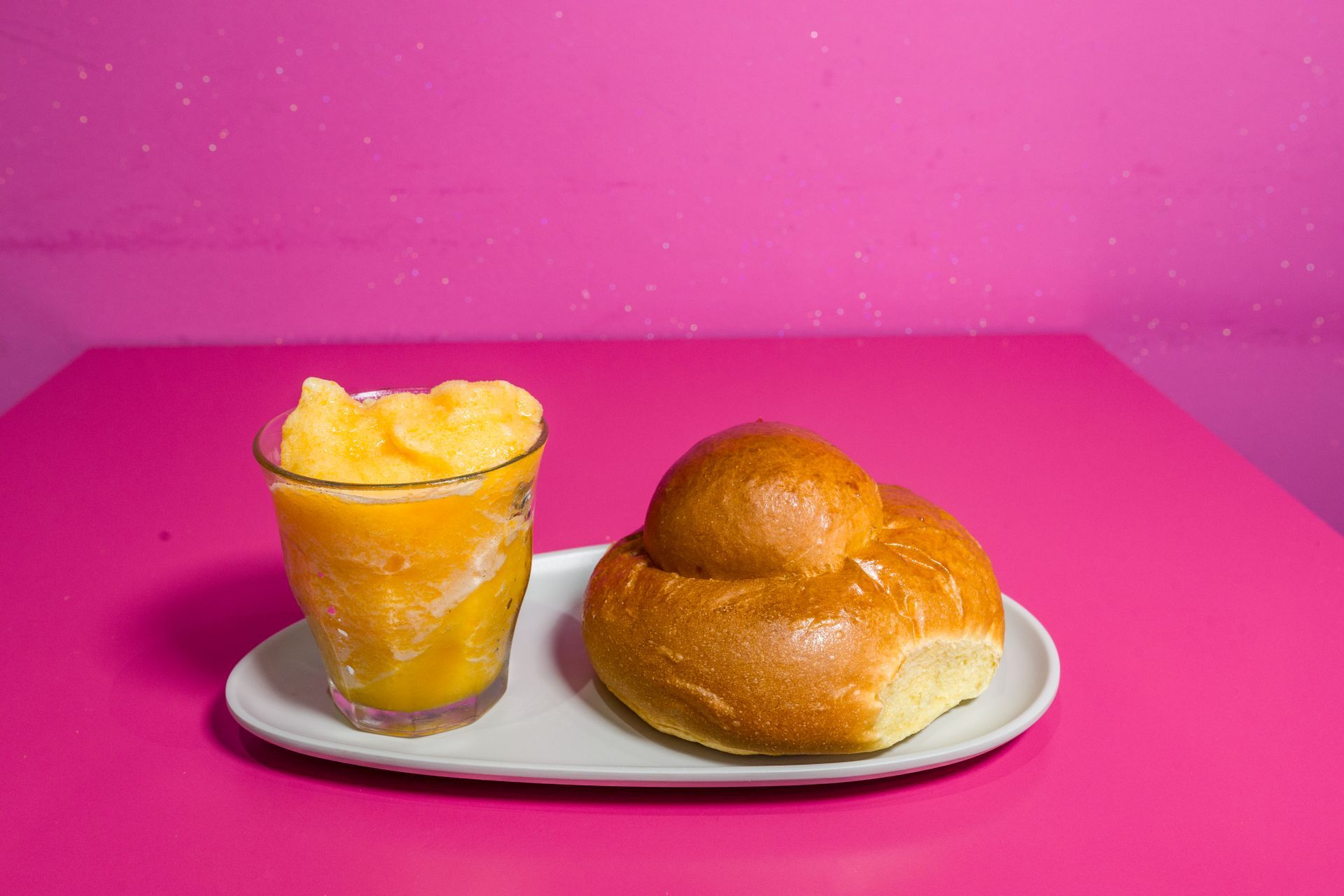 Dessert all'arancia in tazza e un panino glassato su un piatto bianco su uno sfondo rosa acceso.