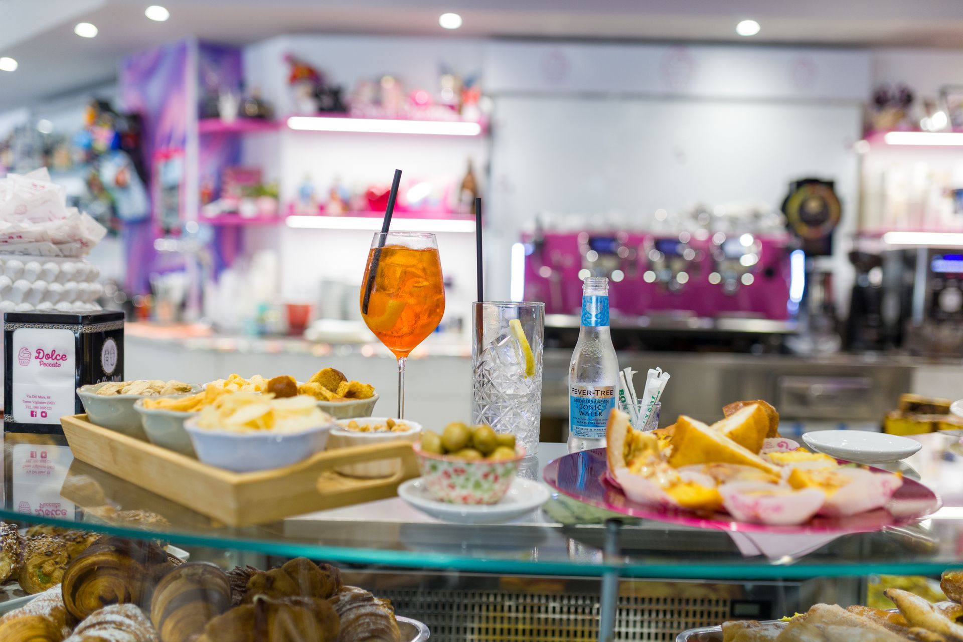 Buffet di dolci con pasticcini, frutta e bevande su un bancone di vetro in un luminoso caffè