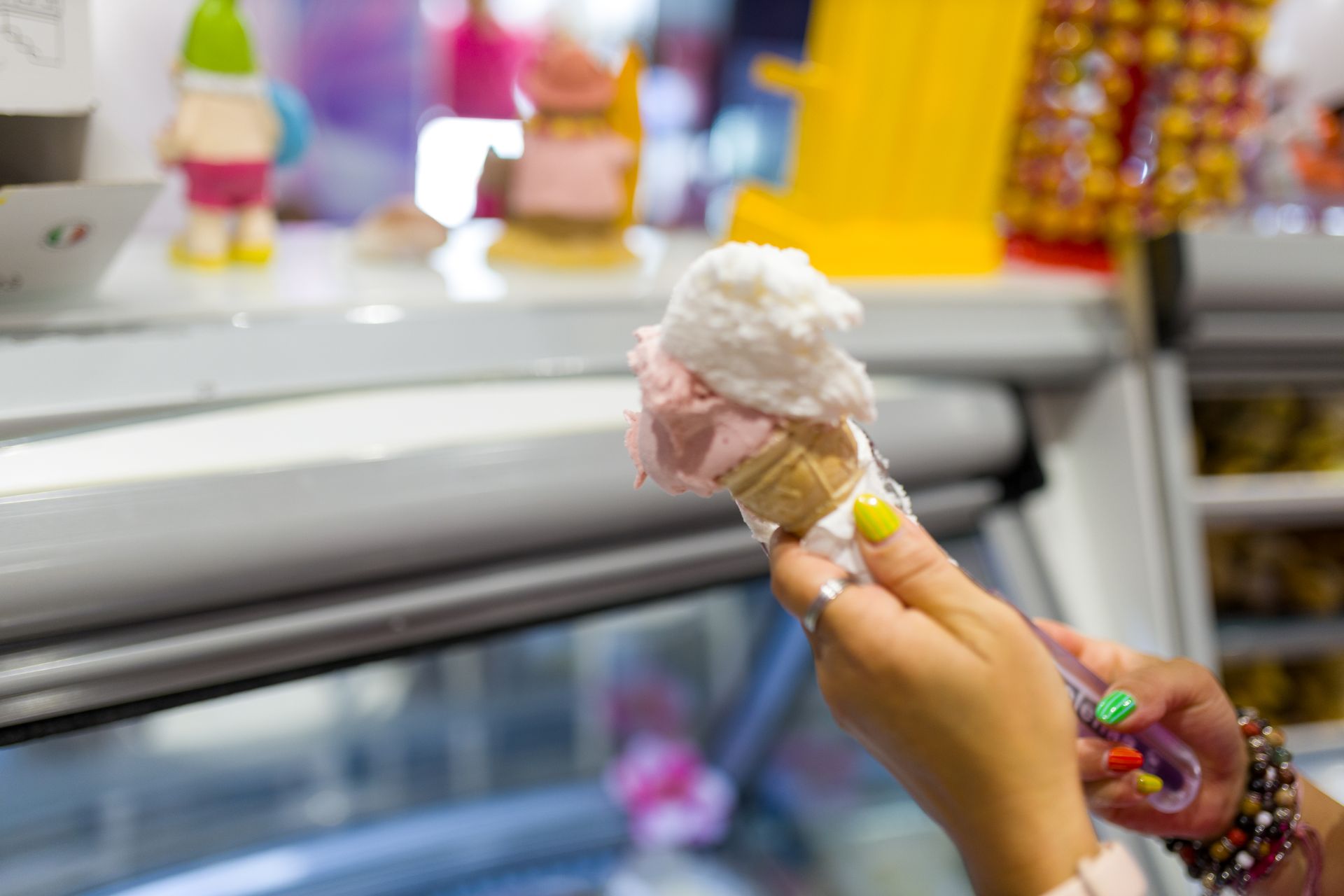 Mano che regge un cono gelato rosa e bianco in una vetrina di un negozio.