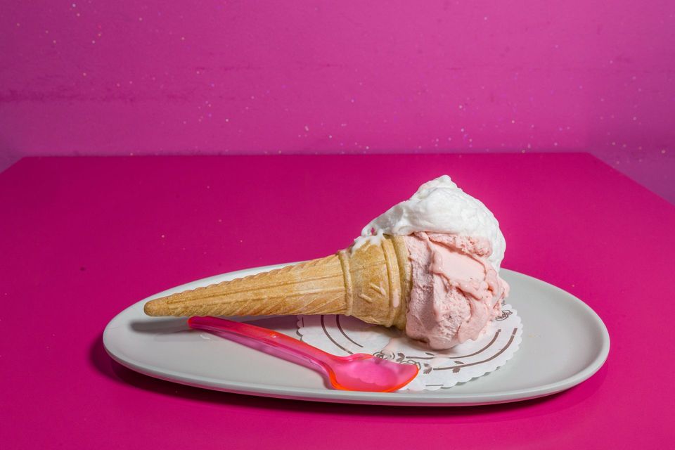 Cono gelato rosa e bianco su un piatto bianco con un cucchiaio rosa su uno sfondo rosa acceso