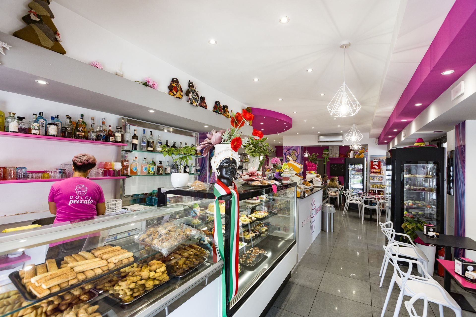 Luminoso interno di panetteria e caffetteria con vetrine, pasticcini, decorazioni colorate e area con posti a sedere.