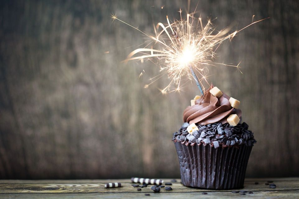 Cupcake al cioccolato con glassa e una stellina scintillante accesa su un tavolo rustico di legno.