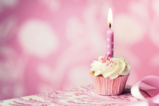 Cupcake di compleanno rosa con glassa bianca e candelina accesa su sfondo rosa.