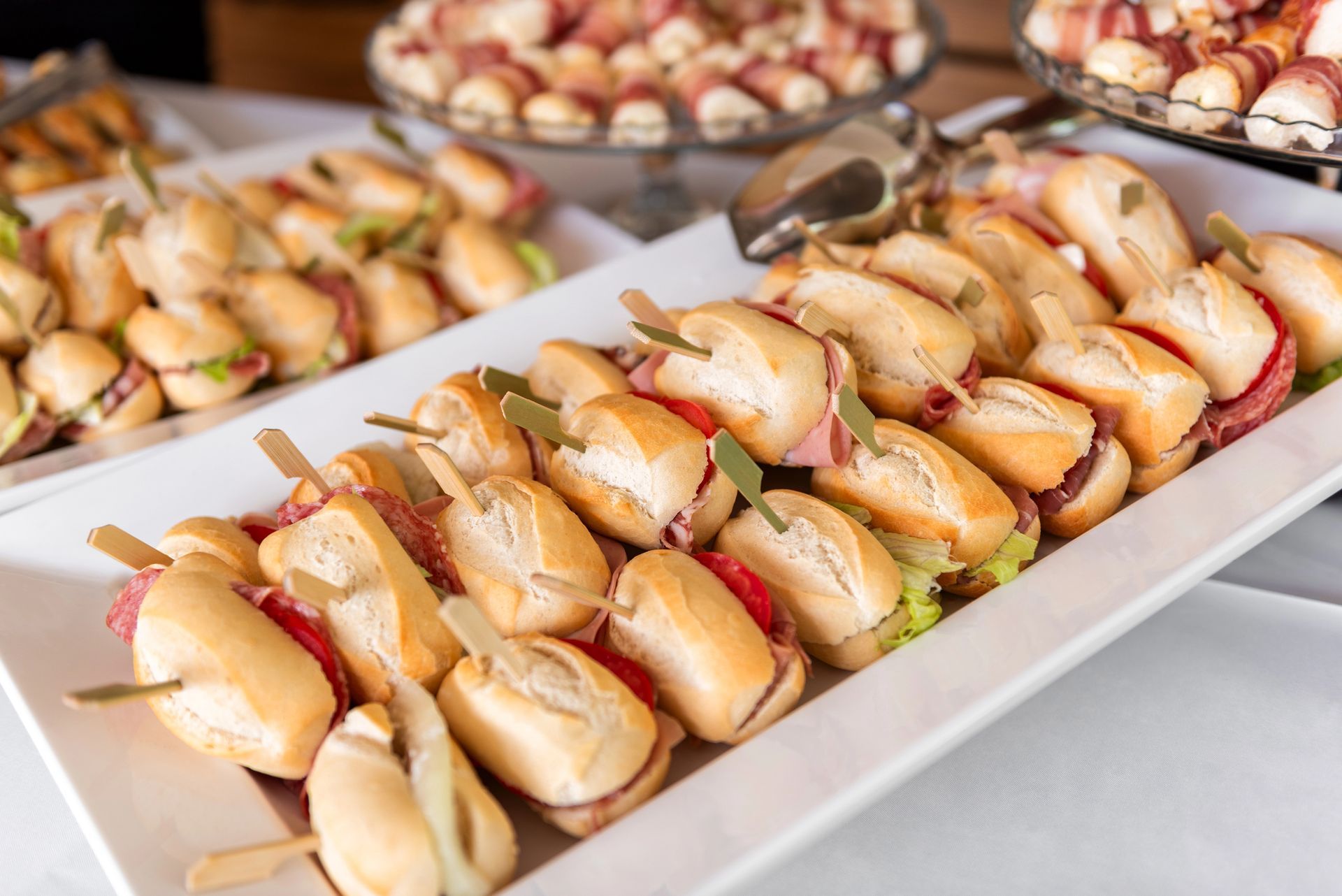 Un vassoio di piccoli panini o mini panini al granchio disposti su un tavolo da buffet, con altri antipasti sullo sfondo.