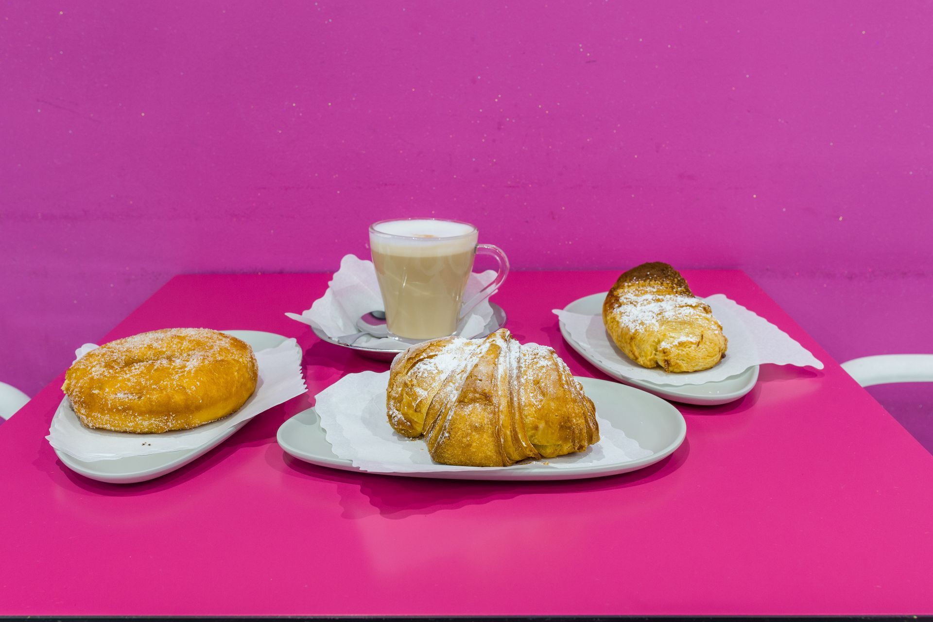 Pasticcini e una tazza di caffè su piatti bianchi su uno sfondo rosa acceso.