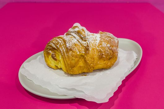 Cornetto con zucchero a velo su un piatto bianco con sfondo rosa acceso.