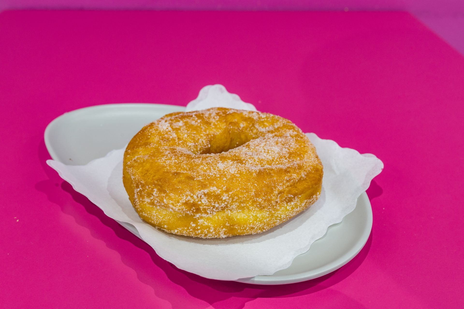 Ciambella ricoperta di zucchero a velo su un piatto bianco, su uno sfondo rosa acceso.