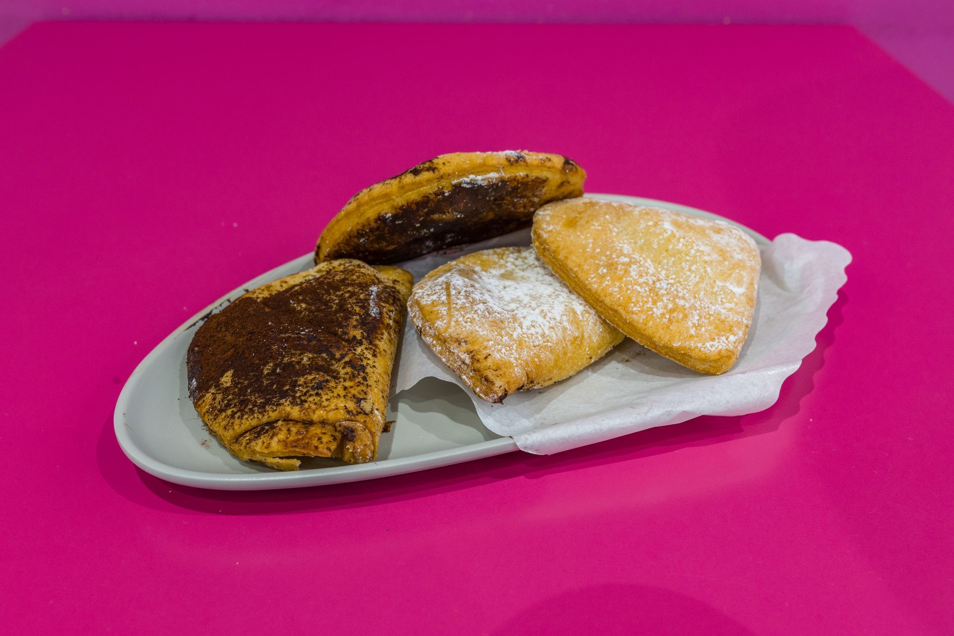 Tre pasticcini assortiti su un piatto bianco su uno sfondo rosa acceso.