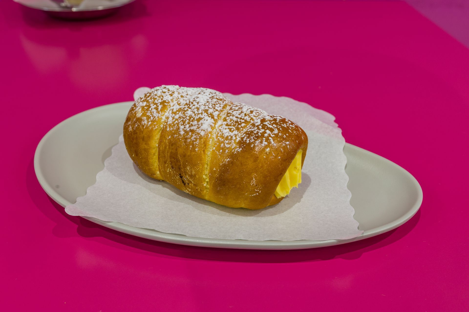 Cannoli di zucchero a velo su un piatto bianco con un tovagliolo su un tavolo rosa acceso.