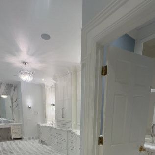 Elegant white bathroom with double vanity, marble-style tile, chandelier, and open door view