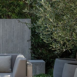 Outdoor patio with gray sofa, concrete planters, and dense green foliage backdrop