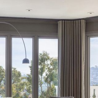 Modern living room with large windows, gray curtains, and a view of trees and a hillside outside