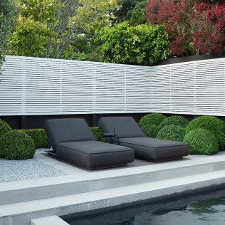 Modern backyard pool with black loungers, white privacy fence, and manicured greenery