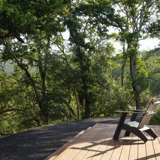 Wooden deck with two chairs overlooking a lush green forest in bright daylight