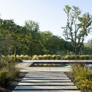 Modern landscaped garden path with striped pavers, ornamental grasses, trees, and a small gazebo