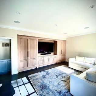 Bright living room with built-in wood cabinets, large TV, white sofa, and sunlit patterned rug