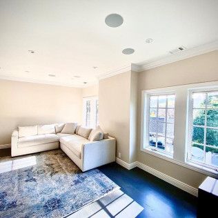 Bright living room with white sectional sofa, blue patterned rug, and large windows on dark wood floor