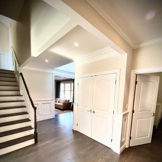 Bright foyer with staircase, double closet doors, and view into a living room with a couch.