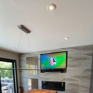 Modern living room with a wall-mounted TV, fireplace, and large windows under a white ceiling
