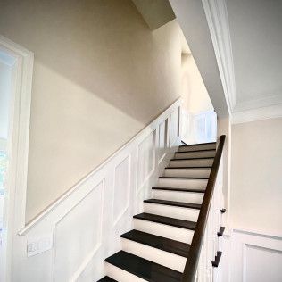 White staircase with dark treads and paneled wall trim in a bright interior hallway