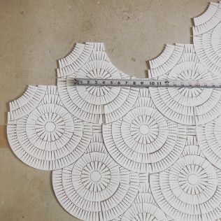 White scalloped lace or embroidery pieces laid out on a beige surface, with a ruler across the top for scale